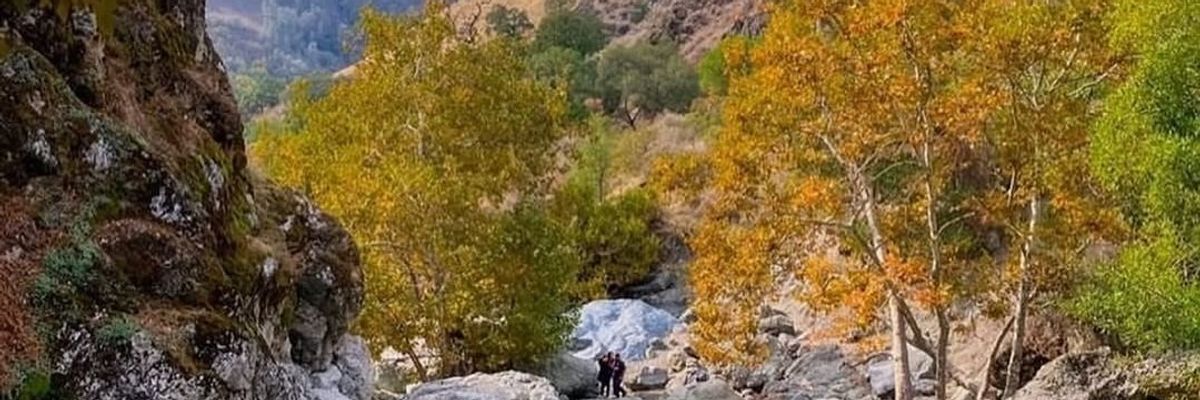Autumn landscape with rocky terrain and colorful trees under a partly cloudy sky.