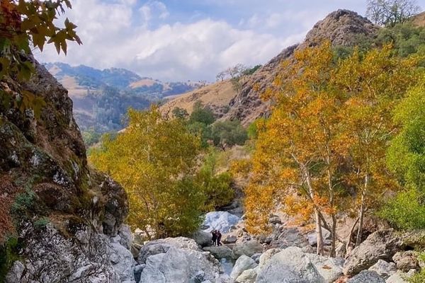 Autumn landscape with rocky terrain and colorful trees under a partly cloudy sky.