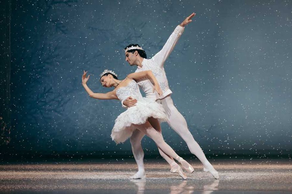 Ballet dancers in white costumes gracefully perform on a snow-covered stage.