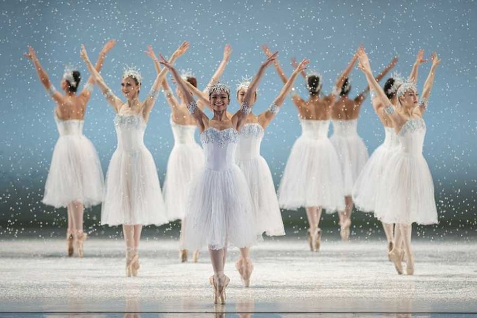 Ballet dancers in white costumes perform on a snowy stage.
