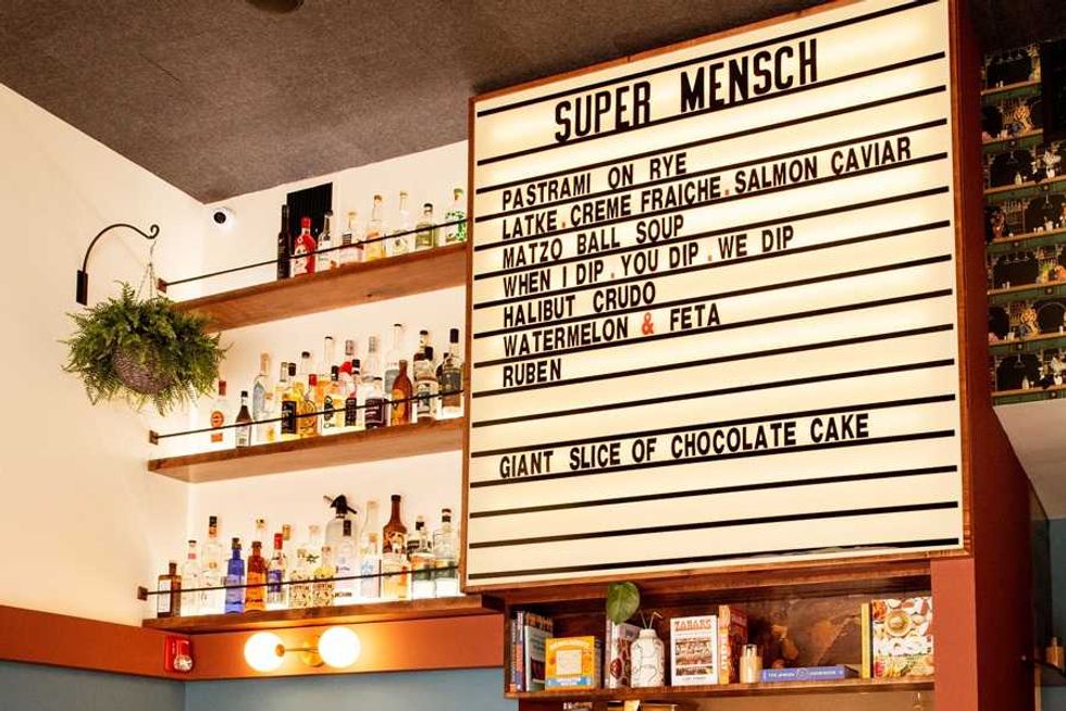Bar menu board with drink shelves, featuring items like Pastrami on Rye and Matzo Ball Soup.