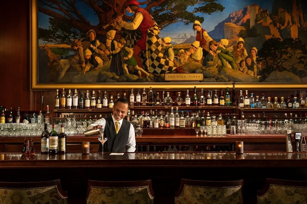 Bartender pouring a drink at a classic bar with a large mural in the background.