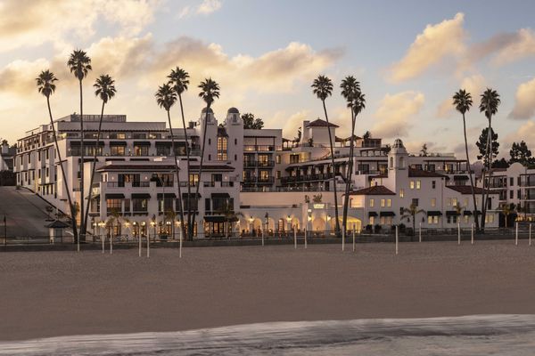 Beachfront hotel with palm trees at sunset, glowing warmly under a cloudy sky.