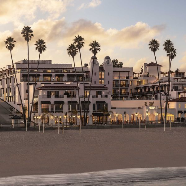 Beachfront hotel with palm trees at sunset, glowing warmly under a cloudy sky.