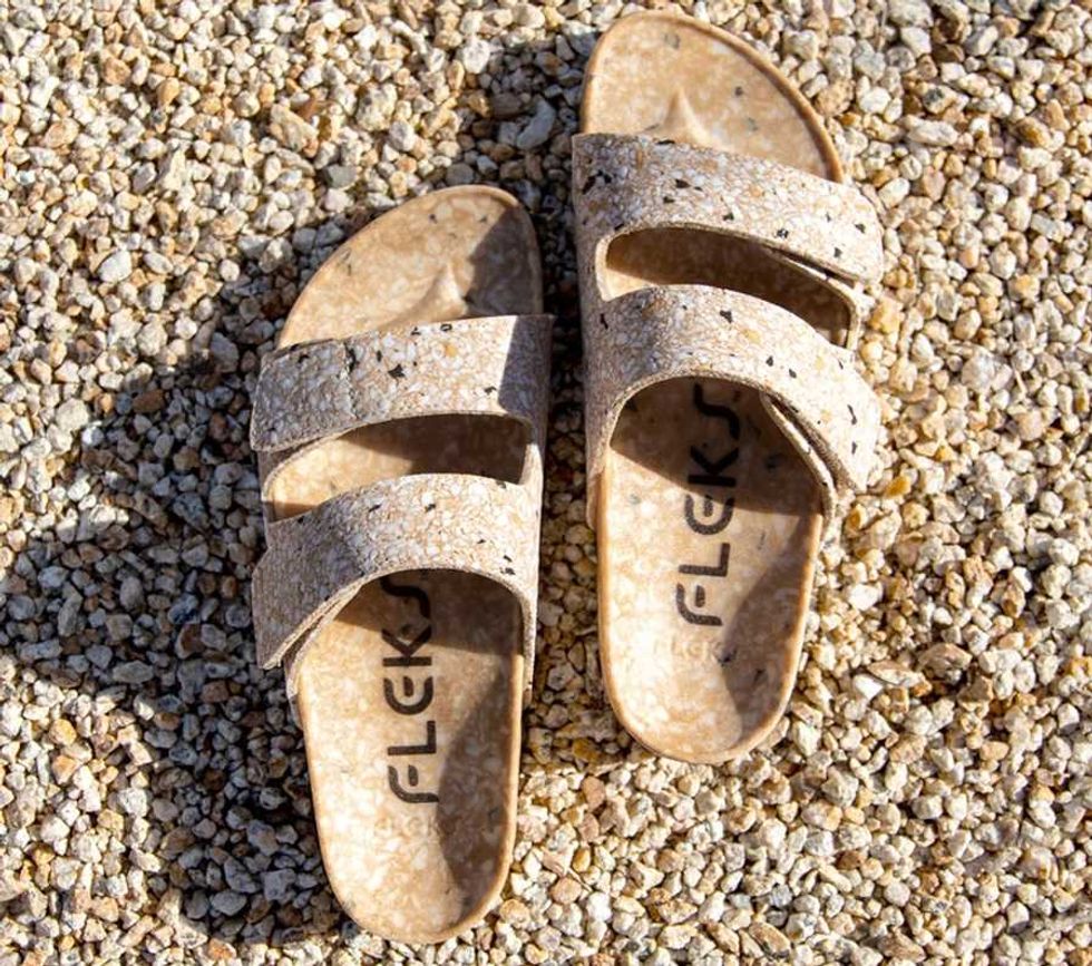 Beige flecked sandals with two straps on a gravel surface.