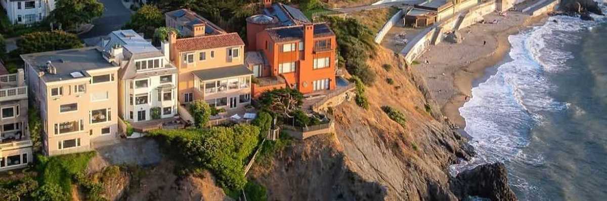 big houses on the edge of a sea cliff with a small beach cove below them