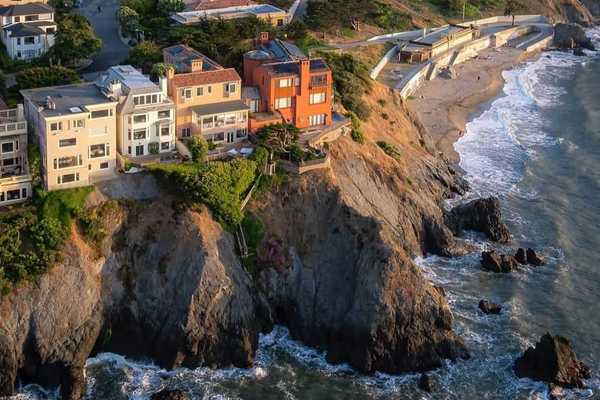 big houses on the edge of a sea cliff with a small beach cove below them