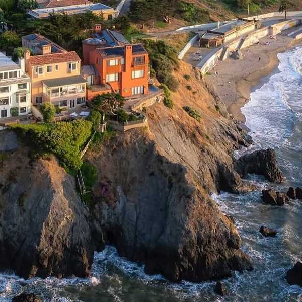 big houses on the edge of a sea cliff with a small beach cove below them