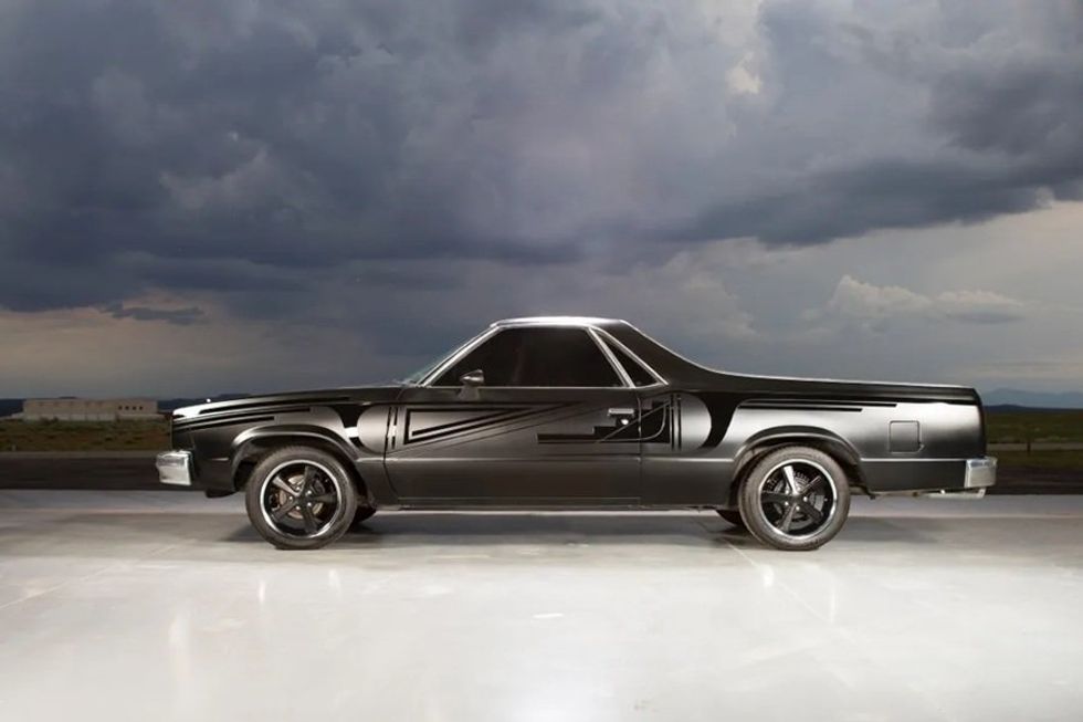 Black sports car with geometric design under stormy skies.