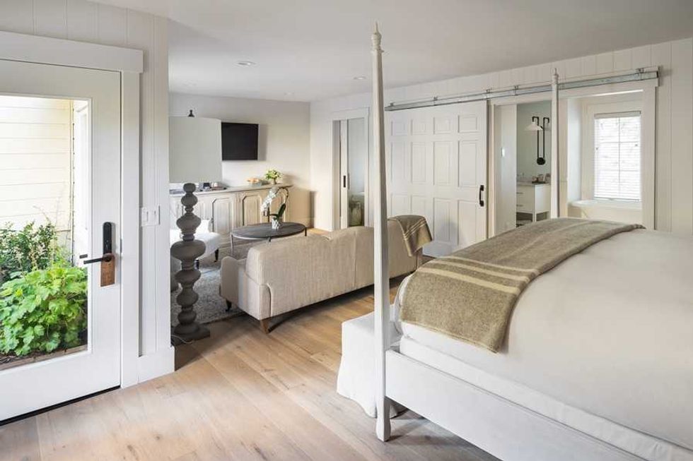 Bright bedroom with a four-poster bed, sliding doors, and a cozy seating area.