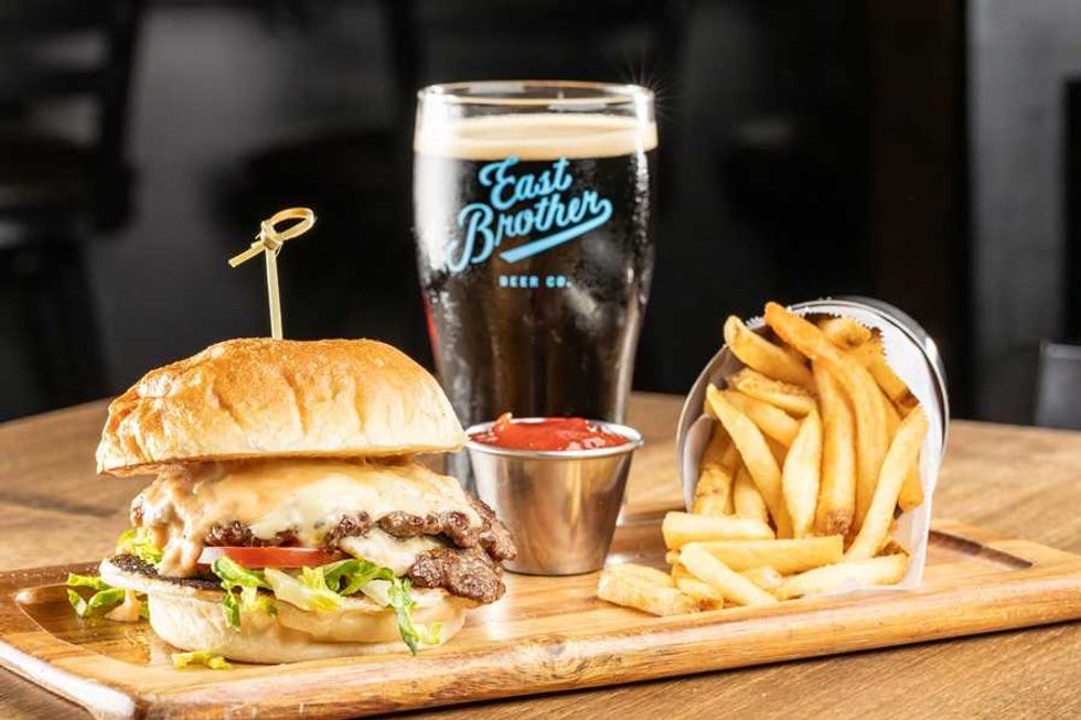 Burger, fries, and dark beer on a wooden board with ketchup.