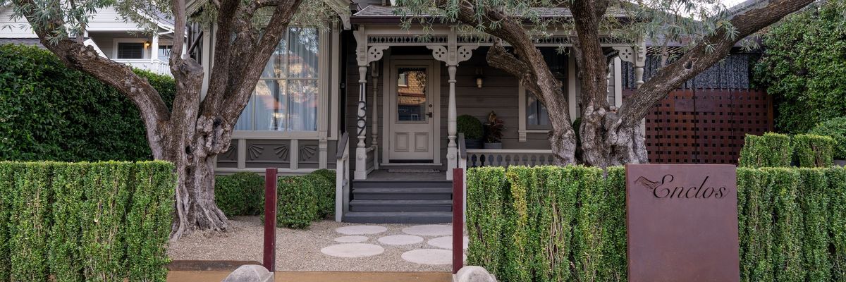 Charming house with large trees and manicured hedges in front.