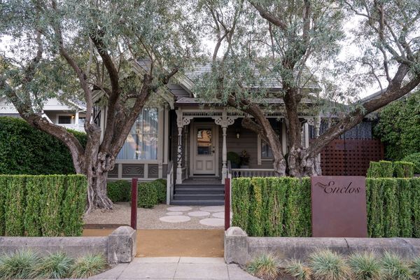 Charming house with large trees and manicured hedges in front.