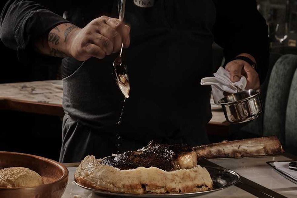 Chef drizzling sauce over a cooked tomahawk steak on a platter.