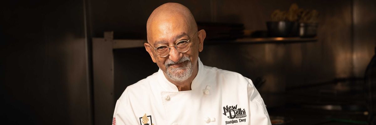 Chef presenting a platter of colorful Indian dishes in a restaurant kitchen.