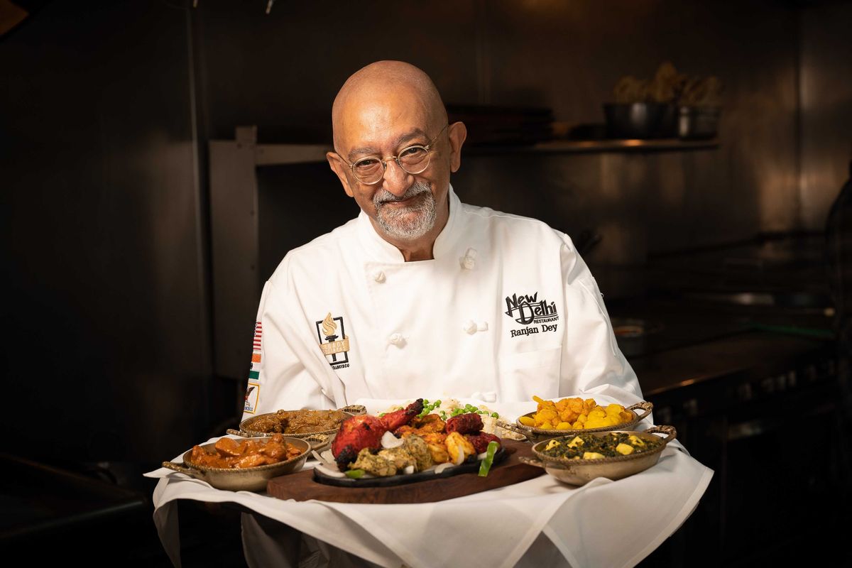 Chef presenting a platter of colorful Indian dishes in a restaurant kitchen.