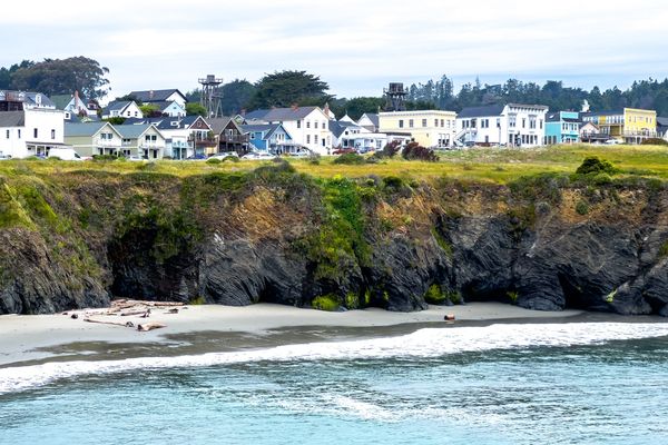 Coastal houses on a cliff above rocky beach with ocean waves.