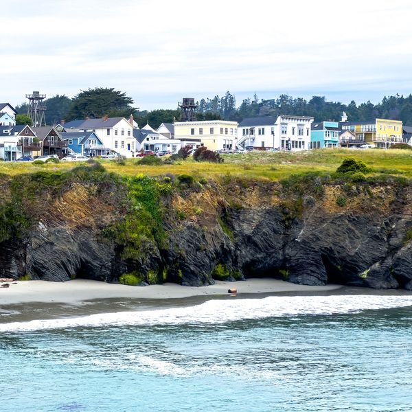 Coastal houses on a cliff above rocky beach with ocean waves.