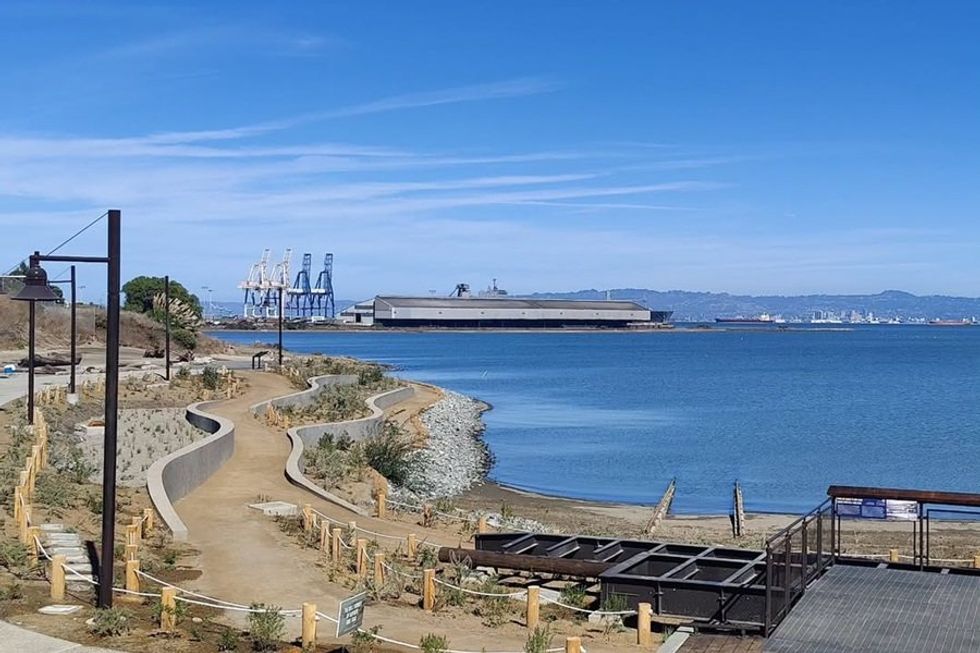 Coastal walkway with industrial cranes and water view under a clear blue sky.