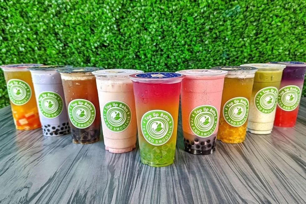 Colorful bubble tea cups on a table, with a green plant wall background.