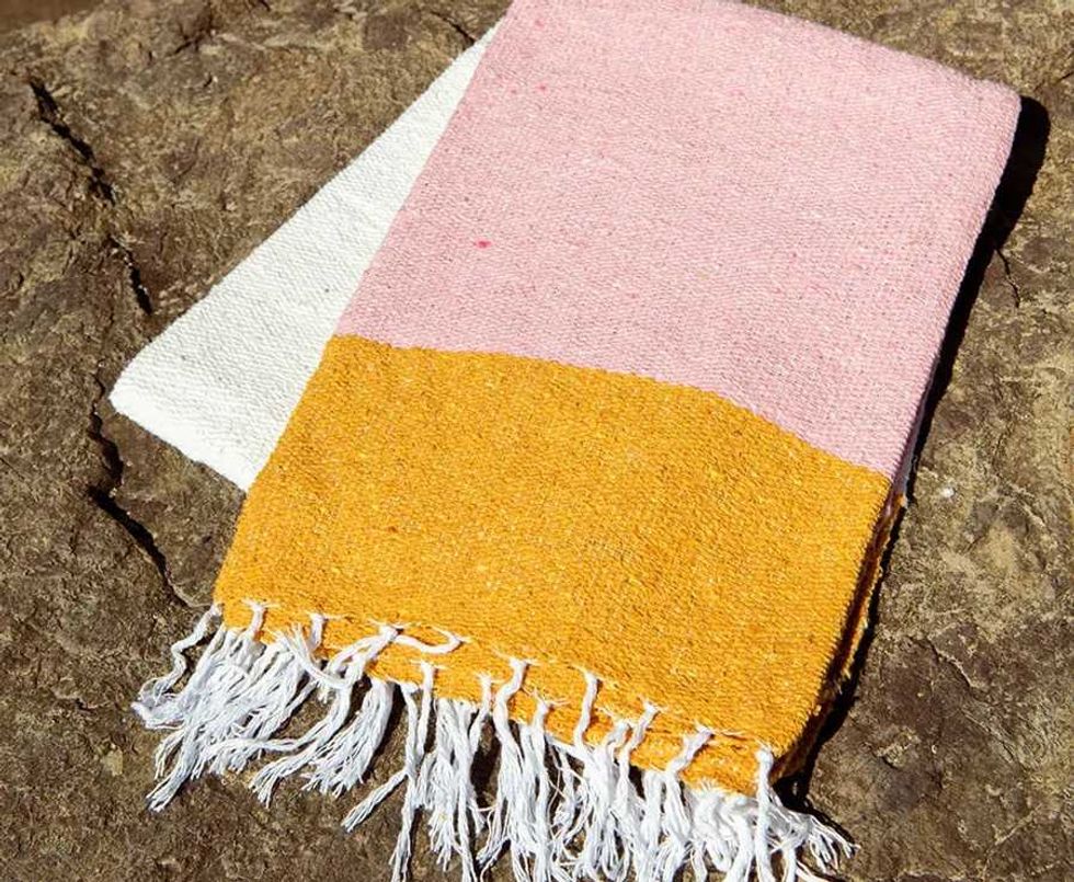 Colorful fringed towel on rocky surface with pink, yellow, and white sections.