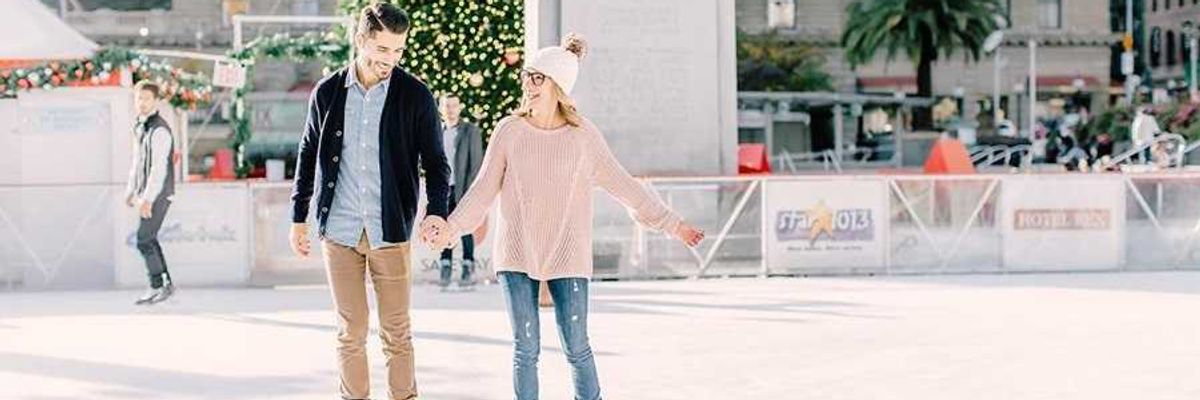 Couple ice skating near a decorated Christmas tree in a city square.