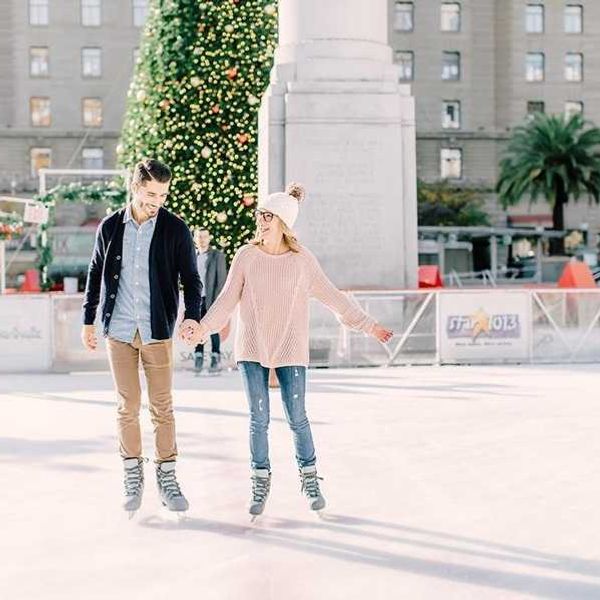 Couple ice skating near a decorated Christmas tree in a city square.