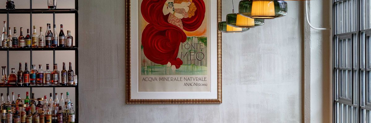 Cozy bar interior with vintage poster, wooden bar stools, and hanging lights.