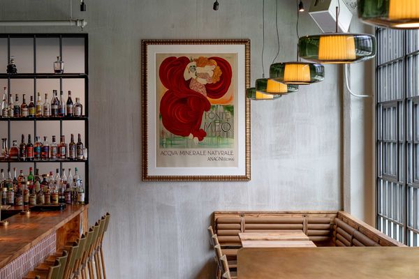 Cozy bar interior with vintage poster, wooden bar stools, and hanging lights.