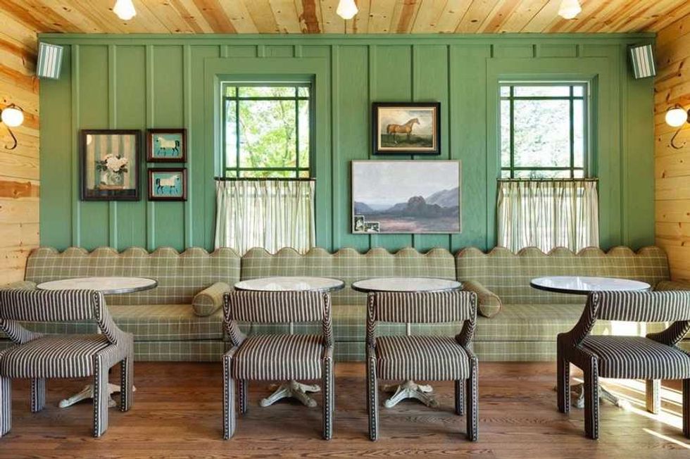 Cozy cafe interior with plaid seating, green walls, and framed art above tables and chairs.
