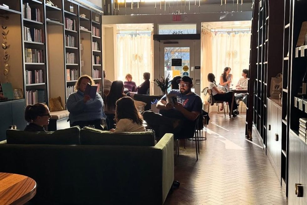 Cozy cafe with people reading and chatting near bookshelves and outdoor light filtering in.
