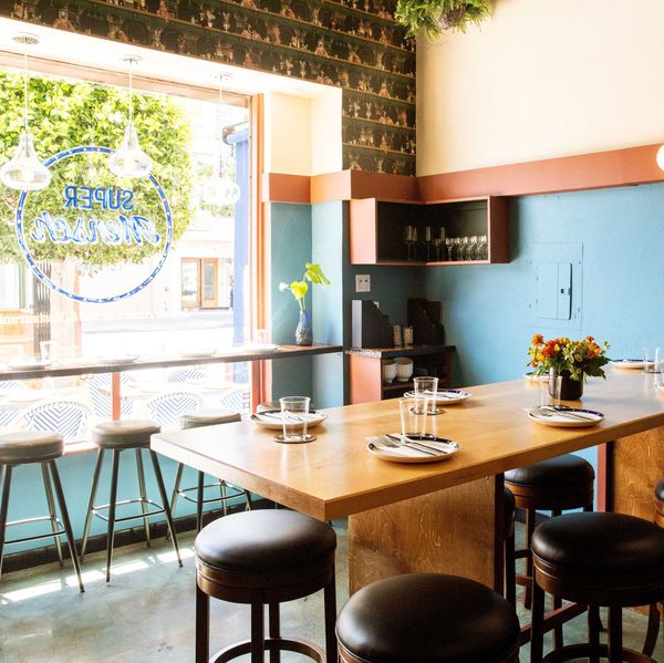 Cozy, modern restaurant interior with wooden table and stools by a large window.