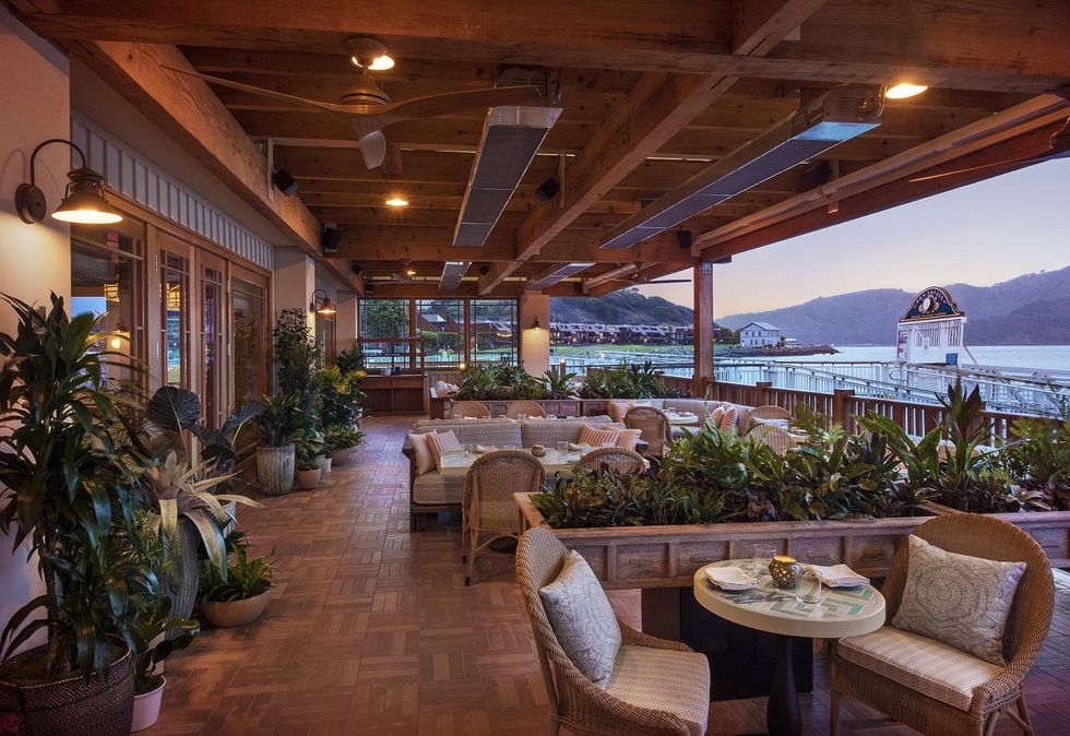 Cozy, plant-filled outdoor dining area overlooking a tranquil bay at sunset.