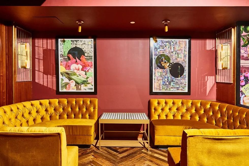 Cozy room with mustard velvet sofas, art on red walls, and a herringbone floor.