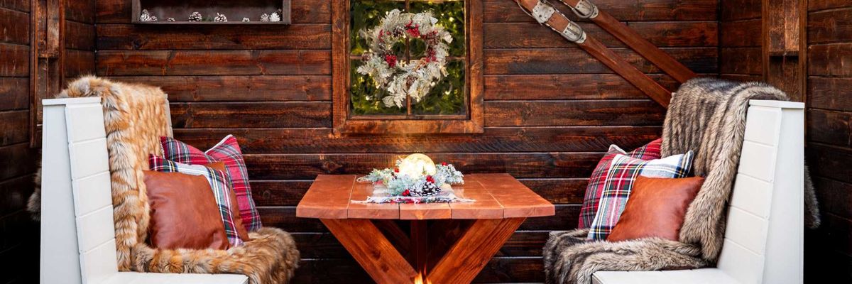 Cozy rustic nook with wood walls, string lights, ski decor, and a central fire pit.