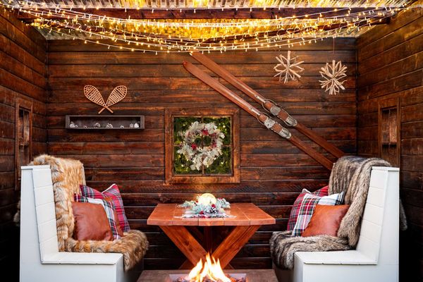 Cozy rustic nook with wood walls, string lights, ski decor, and a central fire pit.