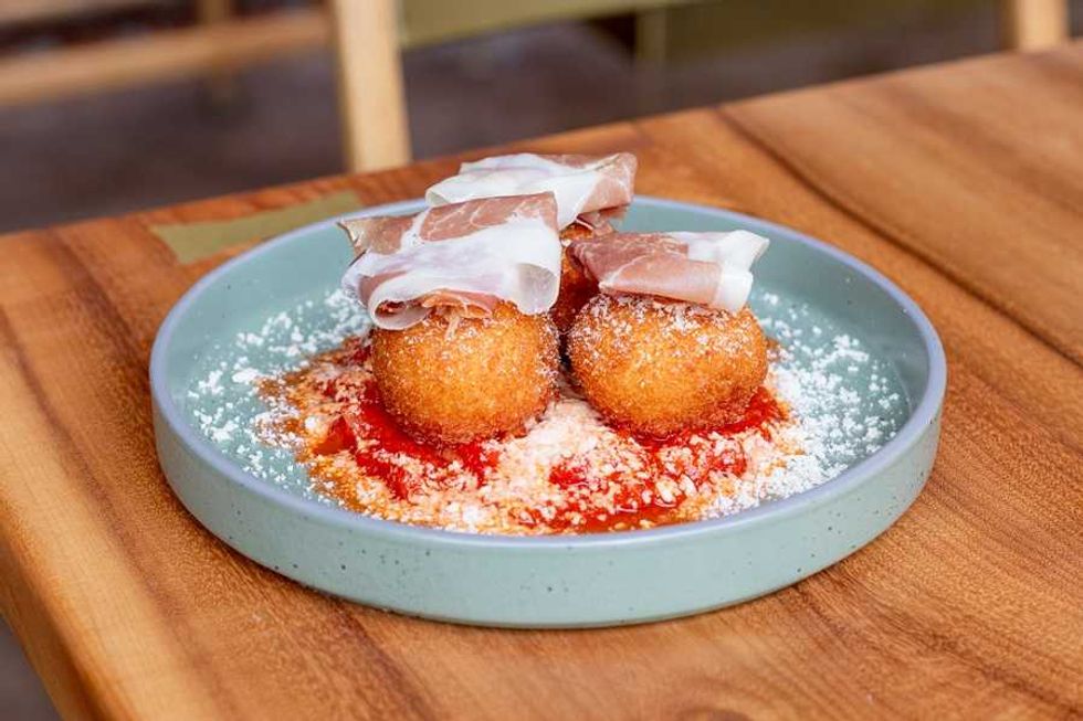 Crispy arancini with prosciutto on a green plate, garnished with tomato sauce and cheese.