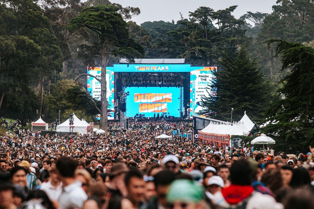 Crowd at Outside Lands festival, with a large stage and trees in the background.