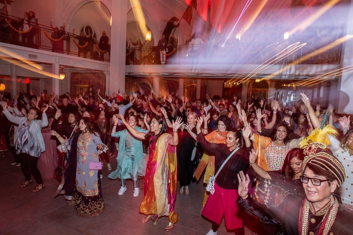 Crowd dancing energetically at a vibrant indoor celebration with colorful lighting.