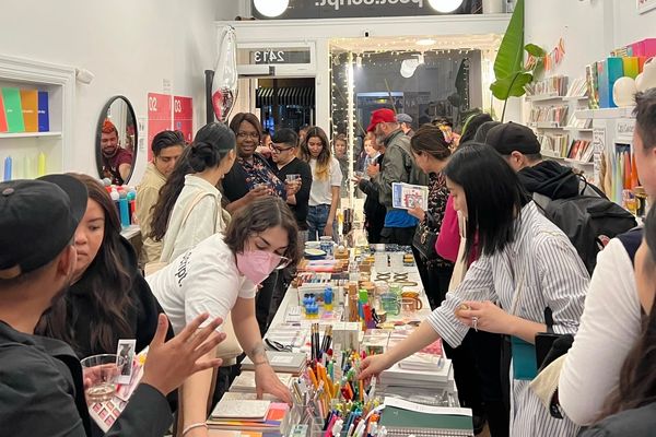 Crowded stationery store with people browsing colorful pens and notebooks.
