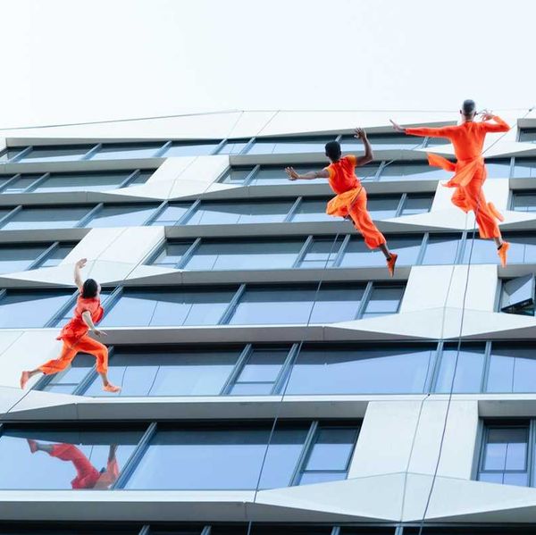 Dancers in orange perform on a building facade, appearing to defy gravity.