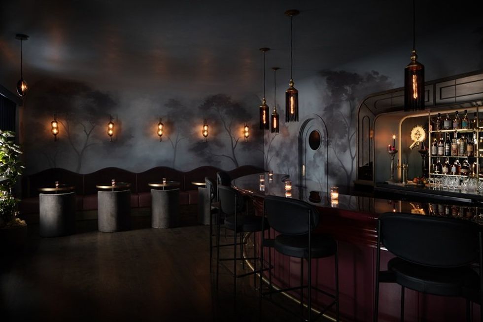 Dimly lit bar with moody d\u00e9cor, mural, and cozy seating.