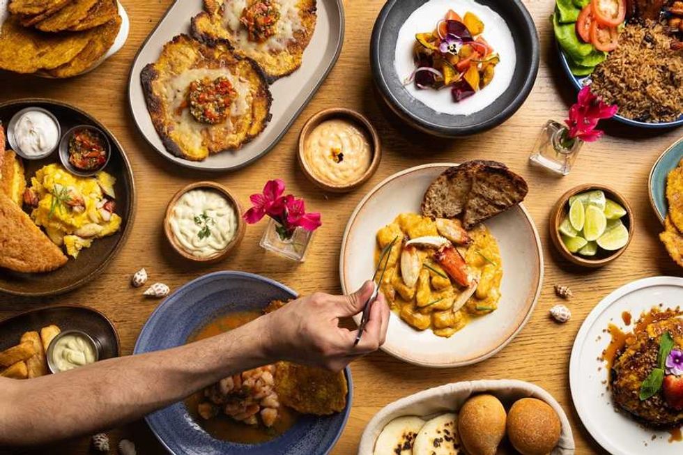 Diverse spread of Latin American dishes on a wooden table, with a hand reaching in.