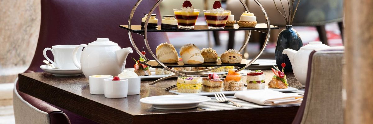 Elegant afternoon tea setup with assorted pastries and a teapot on a wooden table.