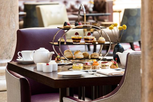 Elegant afternoon tea setup with assorted pastries and a teapot on a wooden table.