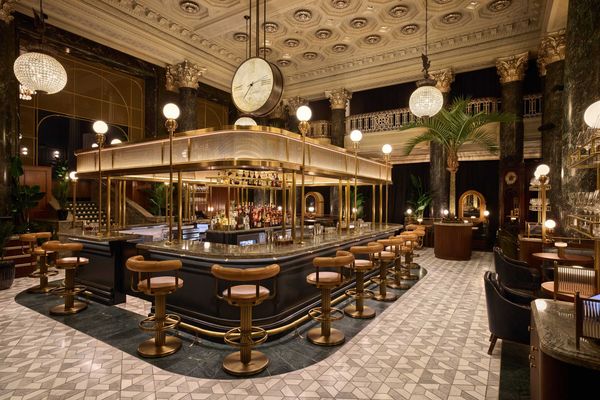 Elegant bar with vintage decor, central clock, and plush seating under ornate chandeliers.