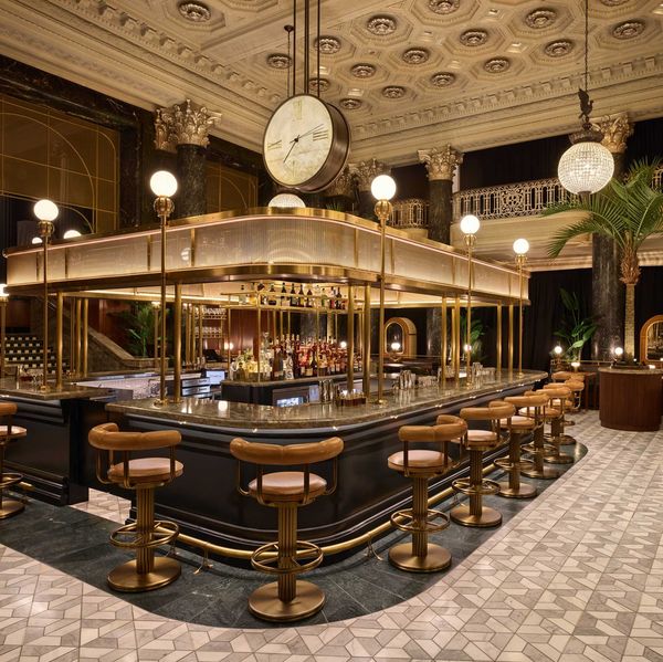 Elegant bar with vintage decor, central clock, and plush seating under ornate chandeliers.