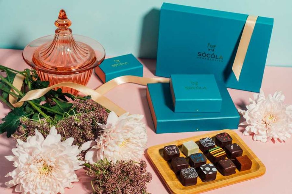 Elegant chocolate boxes, flowers, and glass jar on a pastel pink and blue background.