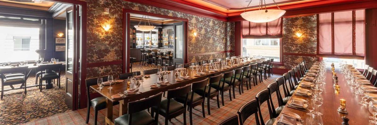 Elegant dining room with long tables set for a formal dinner, warm lighting, and red decor.