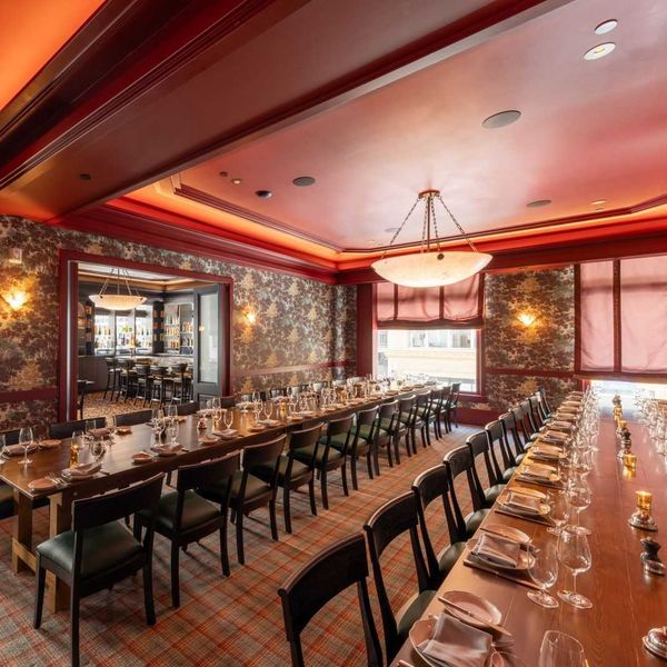 Elegant dining room with long tables set for a formal dinner, warm lighting, and red decor.